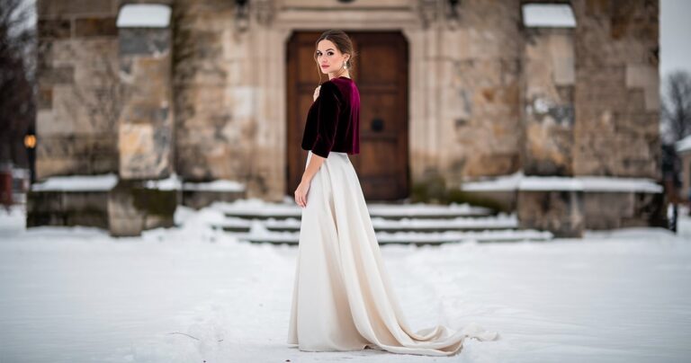 Femme en boléro de velours bordeaux et robe ivoire devant une église en hiver