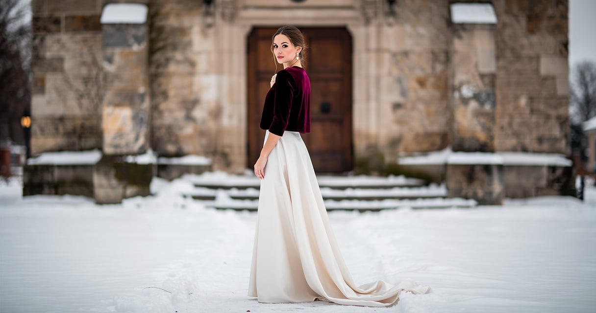 Femme en boléro de velours bordeaux et robe ivoire devant une église en hiver